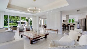 A spacious living area with a large sofa, a coffee table, and a dining table. There is a kitchen area with a refrigerator and bar stools. - Las Palmas 12: 4BR tranquil heaven near golf & beach w/ pool, golf cart, and staff (Punta Cana)