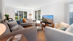 Een moderne woonkamer met een bank, fauteuil, salontafel en een televisie waarop een strandscène te zien is.