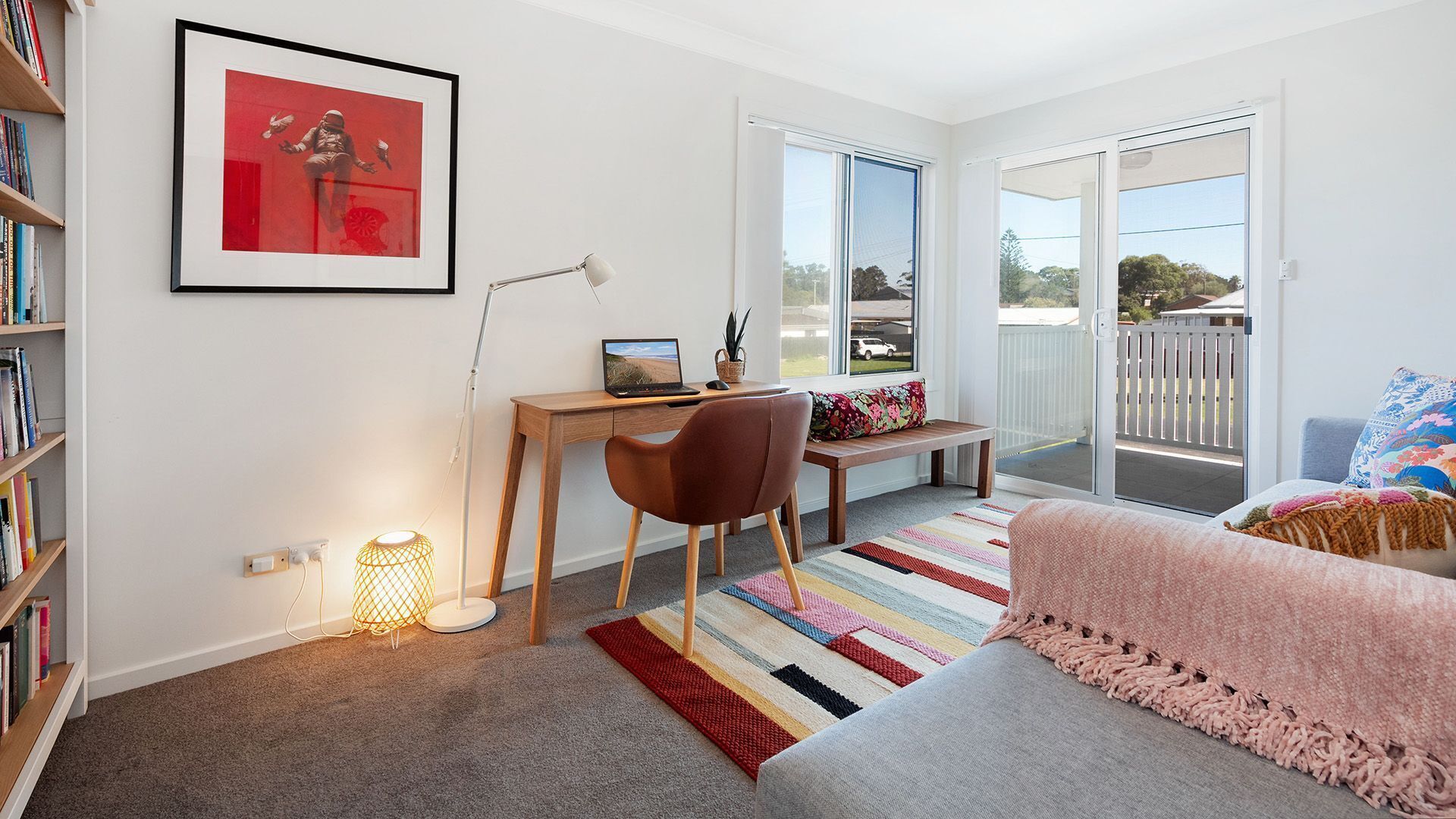 A modern room with a desk, chair, and a sofa. There's a bookshelf, a framed picture, and a window with a view.