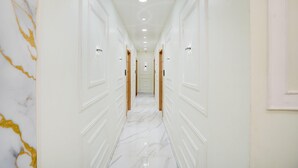 A hallway with white walls, marble flooring, and doors on both sides. - Super Deluxe Room Hotel Ballian's (Prayagraj)