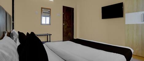 A hotel room with a large bed, a flat-screen TV mounted on the wall, a window, and a wooden wardrobe.