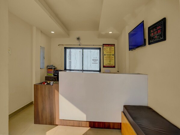A reception area with a wooden reception desk, a blue television, and a digital clock on the wall.
