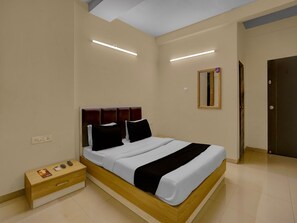A modern bedroom with a wooden bed frame, white bedding, and a bedside table with a phone and remote controls. - Hotel O Vapi Gidc Zion Inn (Vapi)