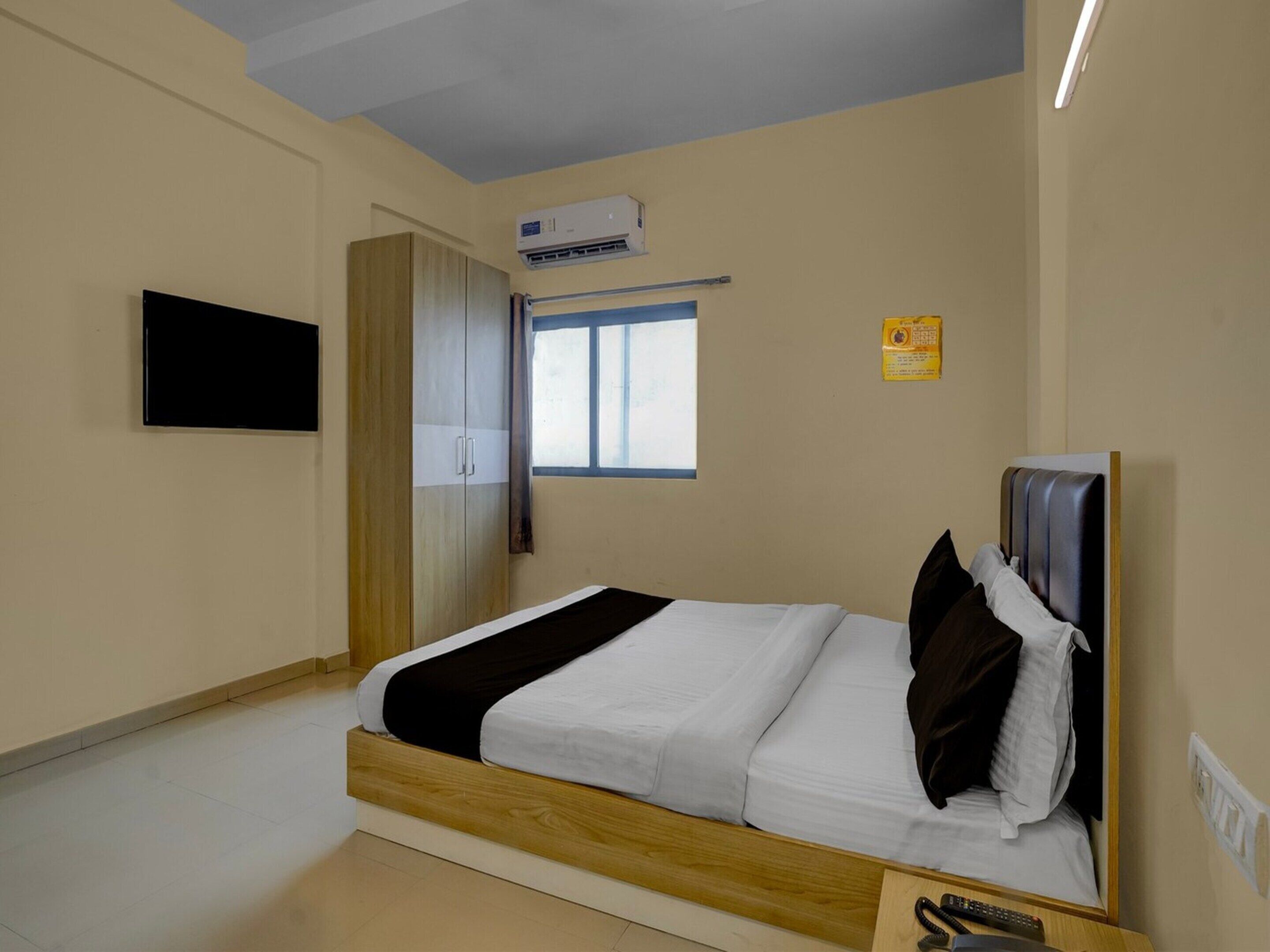 A bedroom with a bed, wardrobe, air conditioning unit, window, and a flat-screen TV.