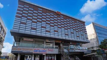 Un immeuble à plusieurs étages abritant divers commerces au rez-de-chaussée, notamment une entreprise de transport, un magasin d’accessoires automobiles et un hôtel.