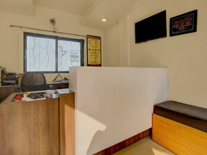 Un espace d’accueil d’hôtel comprenant un comptoir, un banc, un téléviseur et une horloge numérique.