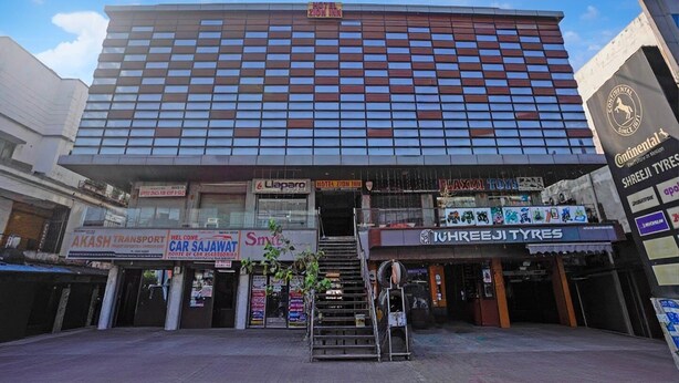A modern hotel with a large glass facade, multiple shops on the ground floor, and a staircase leading to the entrance.