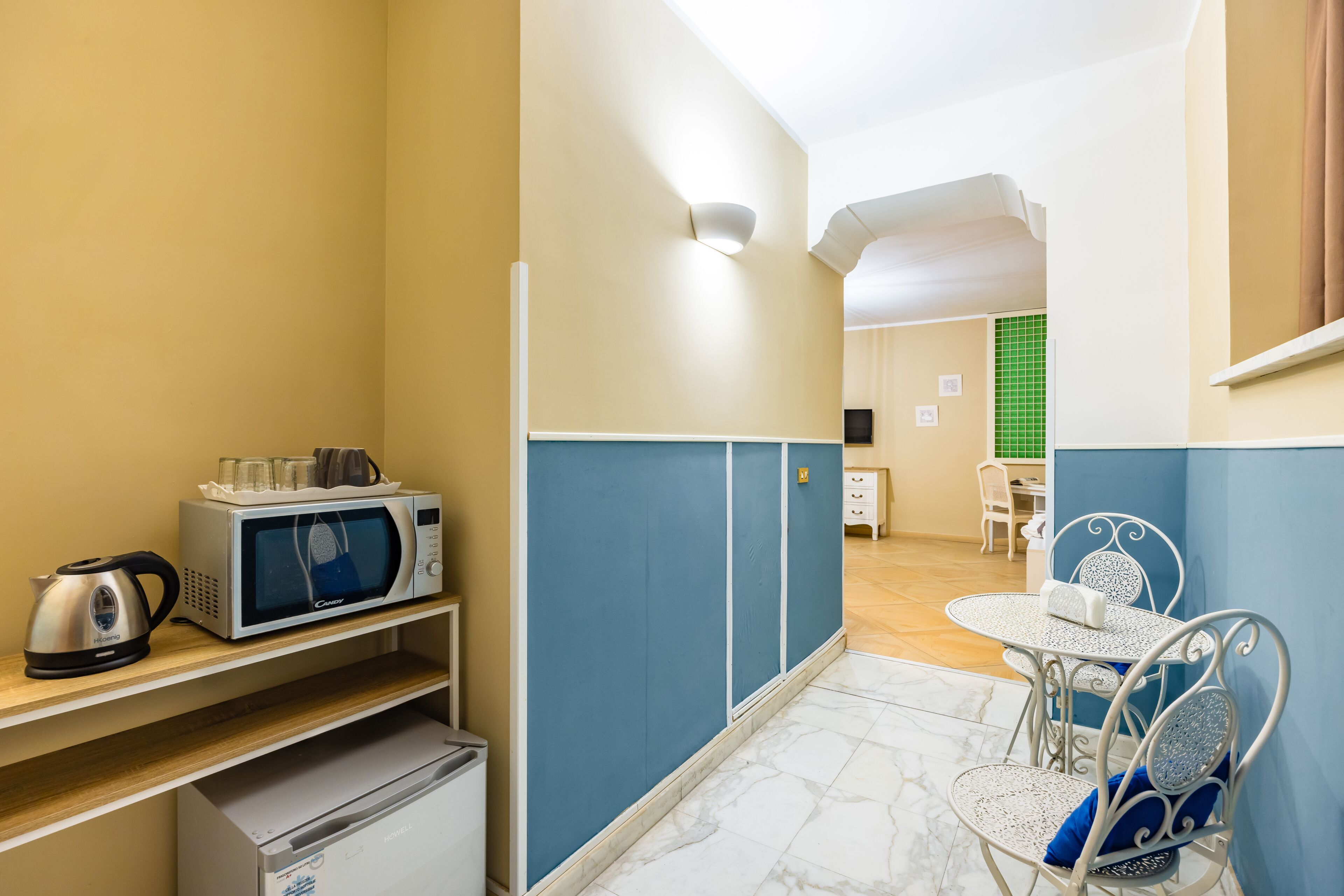 A compact kitchen with a microwave, kettle, and a small refrigerator. There is a dining area with a table and chairs, and a separate seating area with a green wall and a small table.