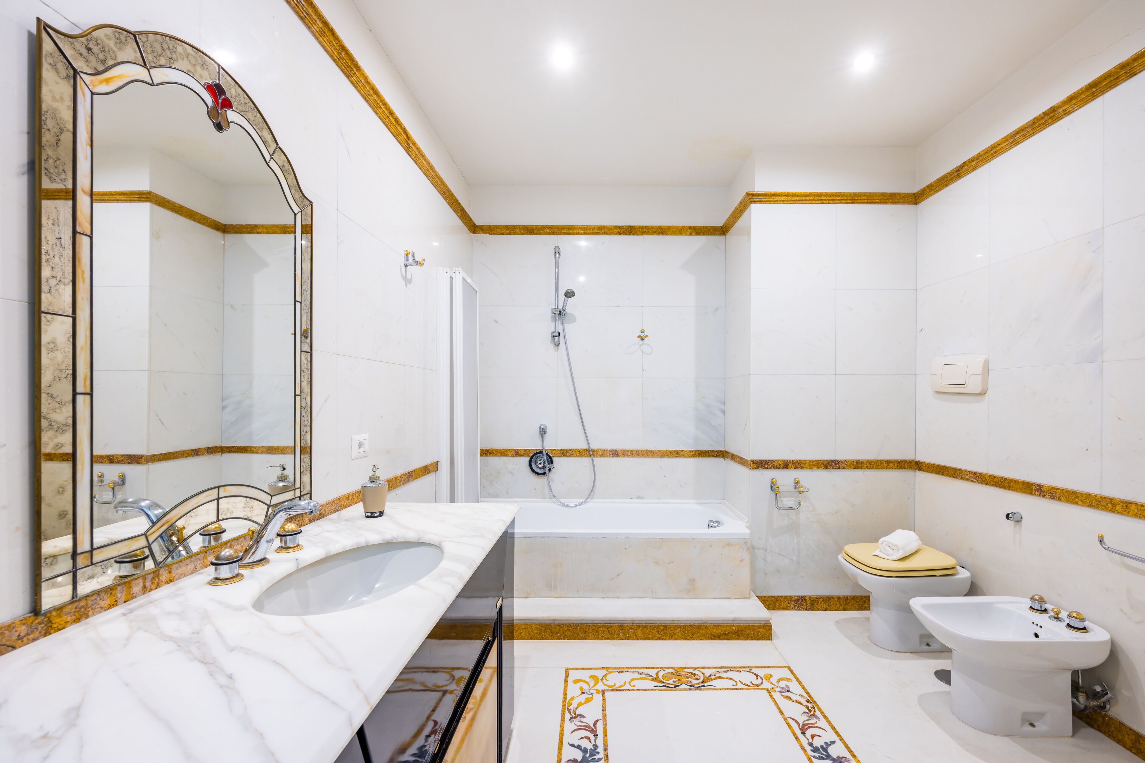 A bathroom with a sink, mirror, bathtub, toilet, and bidet.