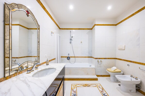Een badkamer met een wastafel, spiegel, bad, toilet en bidet.