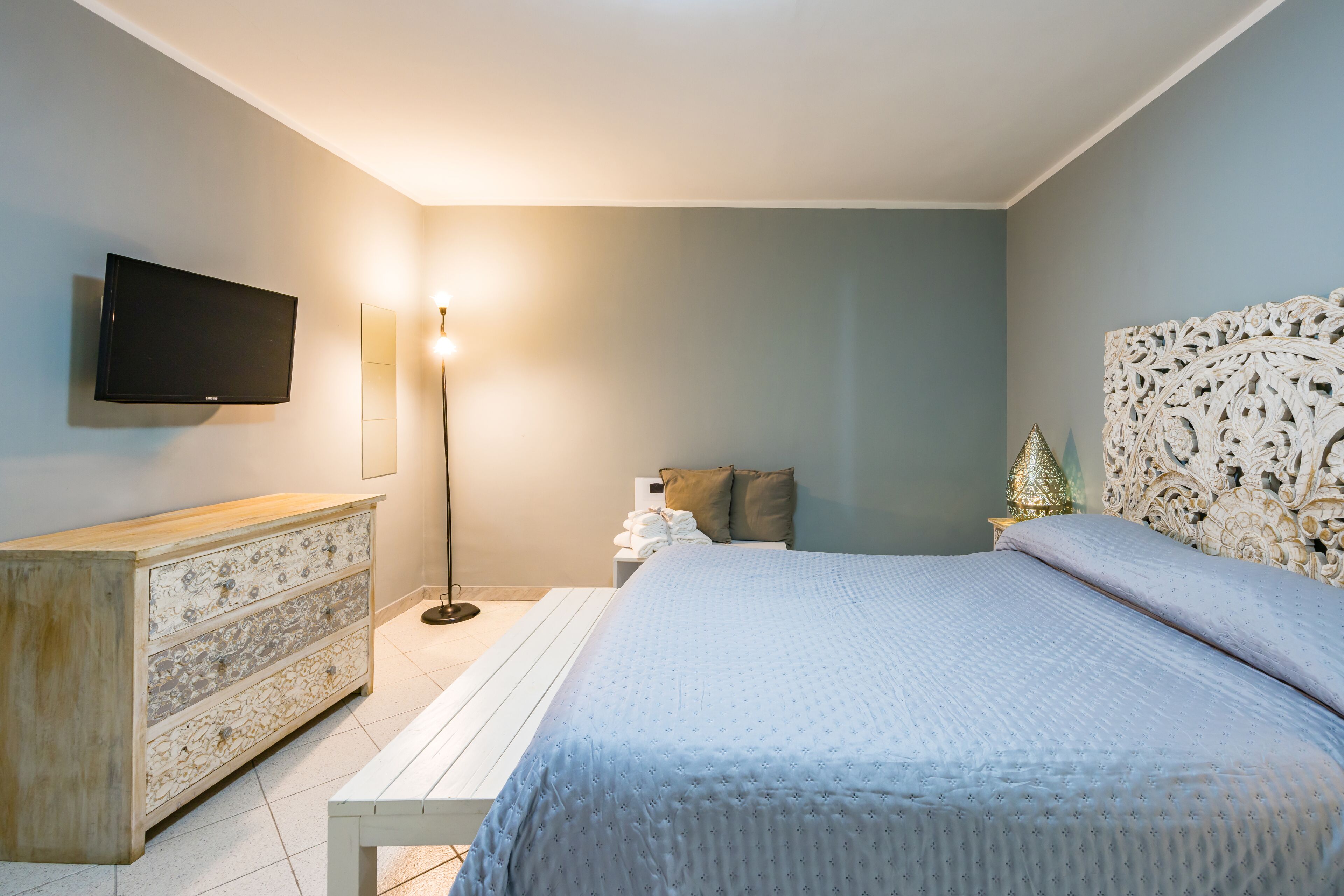 Um quarto com cama, cômoda, televisão e mesa de cabeceira com abajur.