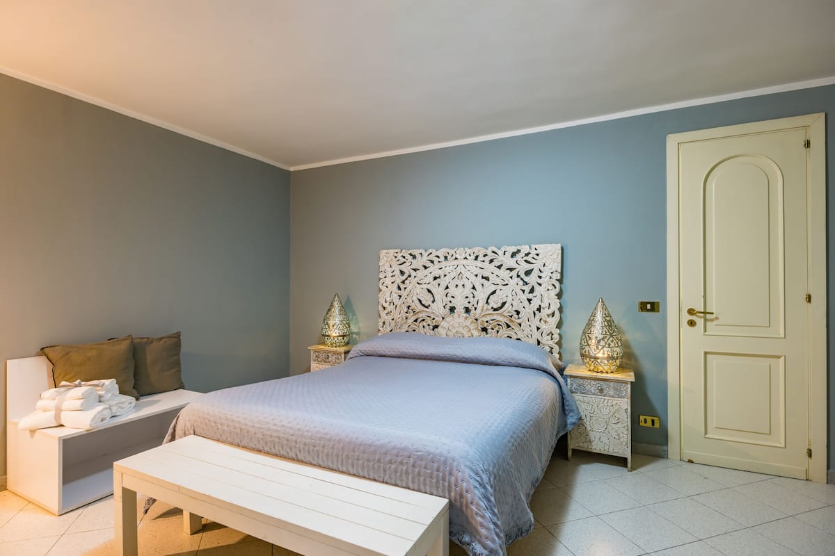 Une chambre à coucher avec un lit, des tables de chevet, un banc et une porte.