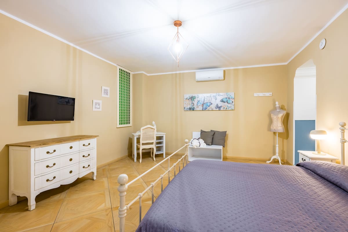 Une chambre à coucher comprenant un lit, une commode, une chaise, un bureau, une lampe et une œuvre d’art accrochée au mur.
