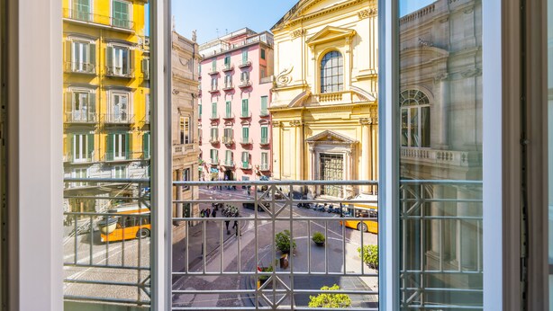 A view through a window of a city street with buildings, a yellow bus, and a pedestrian crossing. - Luxury Toledo 22 (Naples)