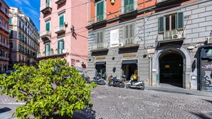 A cobblestone street with parked scooters, a tree, and buildings with balconies and signage. - Luxury Toledo 22 (Naples)
