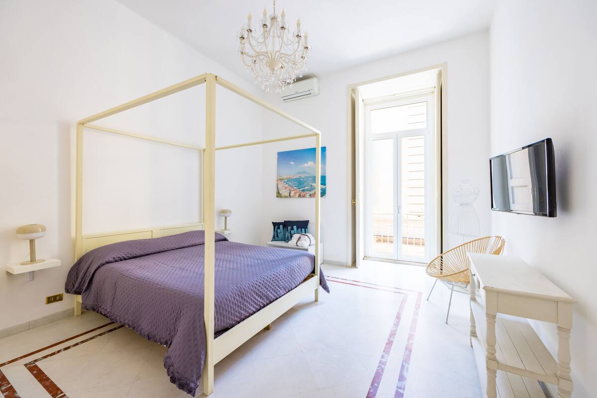 Une chambre à coucher avec un lit à baldaquin, un bureau, une chaise, un lustre et un tableau accroché au mur.