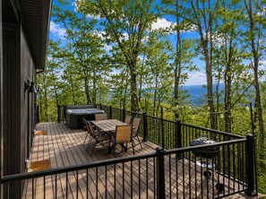 Una terraza con jacuzzi, mesa y sillas, rodeada de árboles y vistas al paisaje.