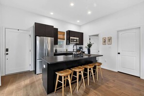 Una cocina moderna con una isla central, electrodomésticos de acero inoxidable y taburetes de madera.