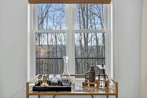 A room with a large window, a table with glassware and a coffee maker, and a view of leafless trees. - Modern Cabin Retreat w Hot Tub, Sauna & Fire Pit (Great Cacapon)