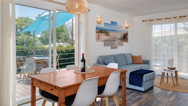 A modern living room with a wooden dining table, white chairs, a blue sofa, and a large window. - Holiday Home 'Lacaducee' with Balcony, Wi-Fi and Air Conditioning (Peujard)