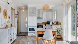 A modern kitchen with white cabinets, a dining area with a wooden table and chairs, and a large window with a view of greenery. - Holiday Home 'Lacaducee' with Balcony, Wi-Fi and Air Conditioning (Peujard)