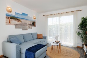 A modern living room with a light blue sofa, a small round table, and a large window with sheer curtains.