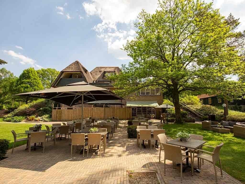 An outdoor patio area with tables and chairs, a wooden fence, and a large tree.
