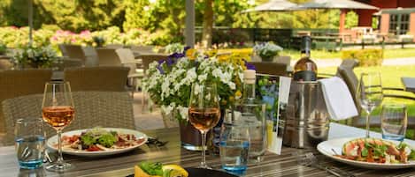 An outdoor dining table with plates of food, wine glasses, and a vase of flowers.