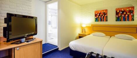 Ein Hotelzimmer mit Fernseher, Bett, Nachttisch, Lampe und einem Kunstwerk an der Wand.
