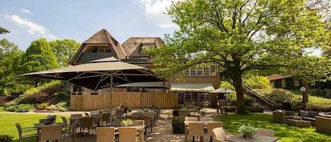 An outdoor patio area with tables and chairs, a wooden fence, and a large tree.