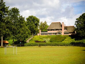 Ein großes Gebäude mit einem Strohdach, umgeben von üppiger Vegetation und einem gepflegten Rasen.