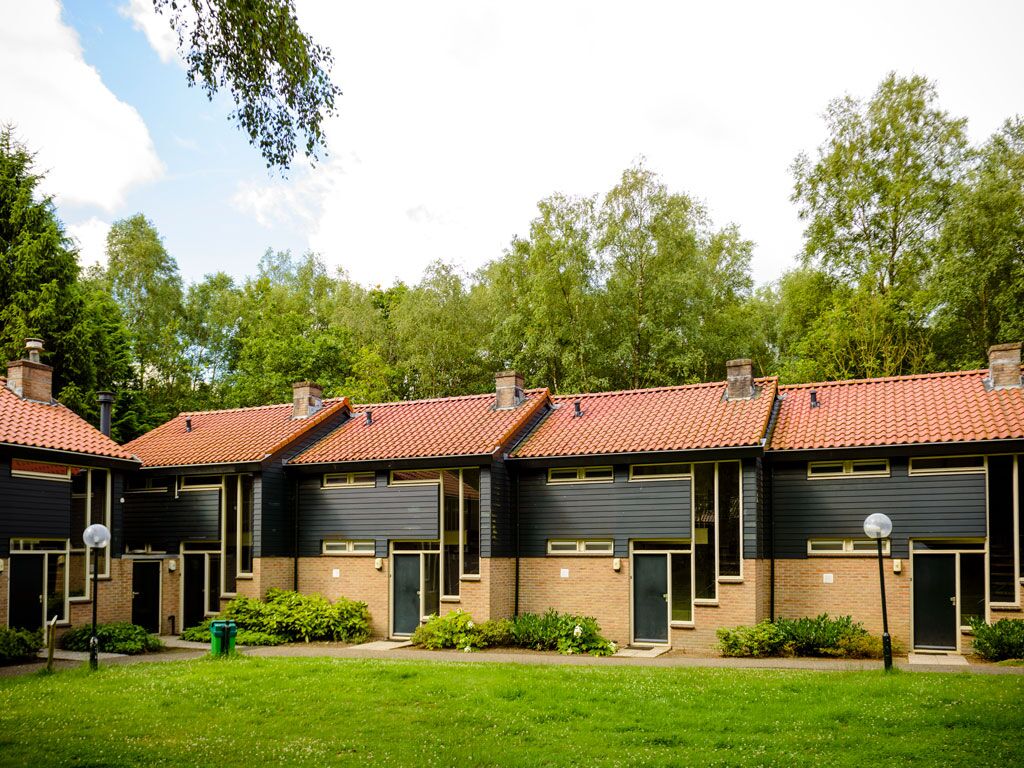 A row of modern buildings with brick and dark siding, red-tiled roofs, and a green lawn.
