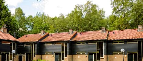 A row of modern buildings with brick and dark siding, red-tiled roofs, and a green lawn.