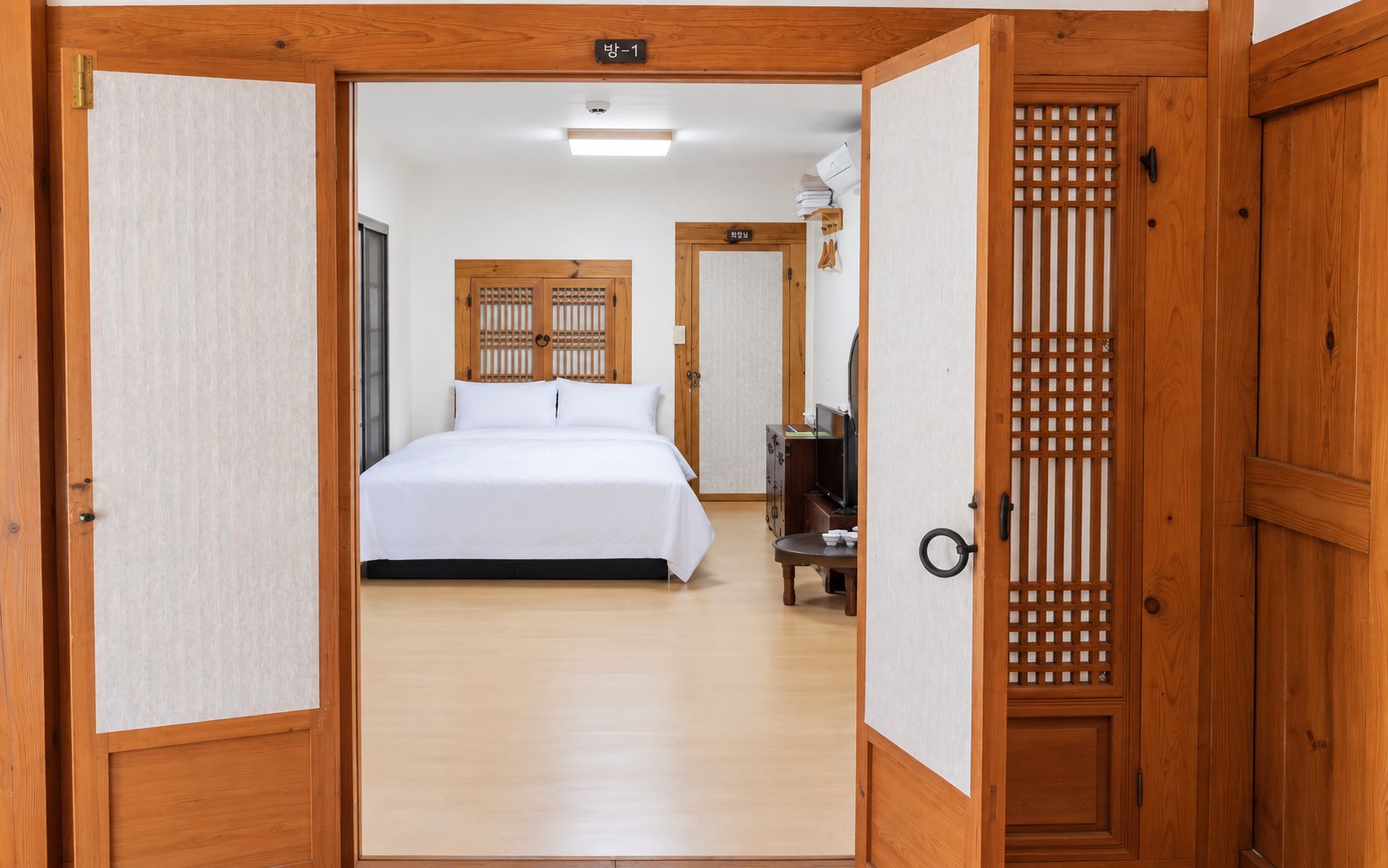 A hotel room with a bed, a desk, and a traditional wooden door.