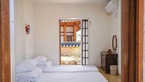 A room with two beds, a wooden cabinet, a trash bin, and a view of a traditional building outside.