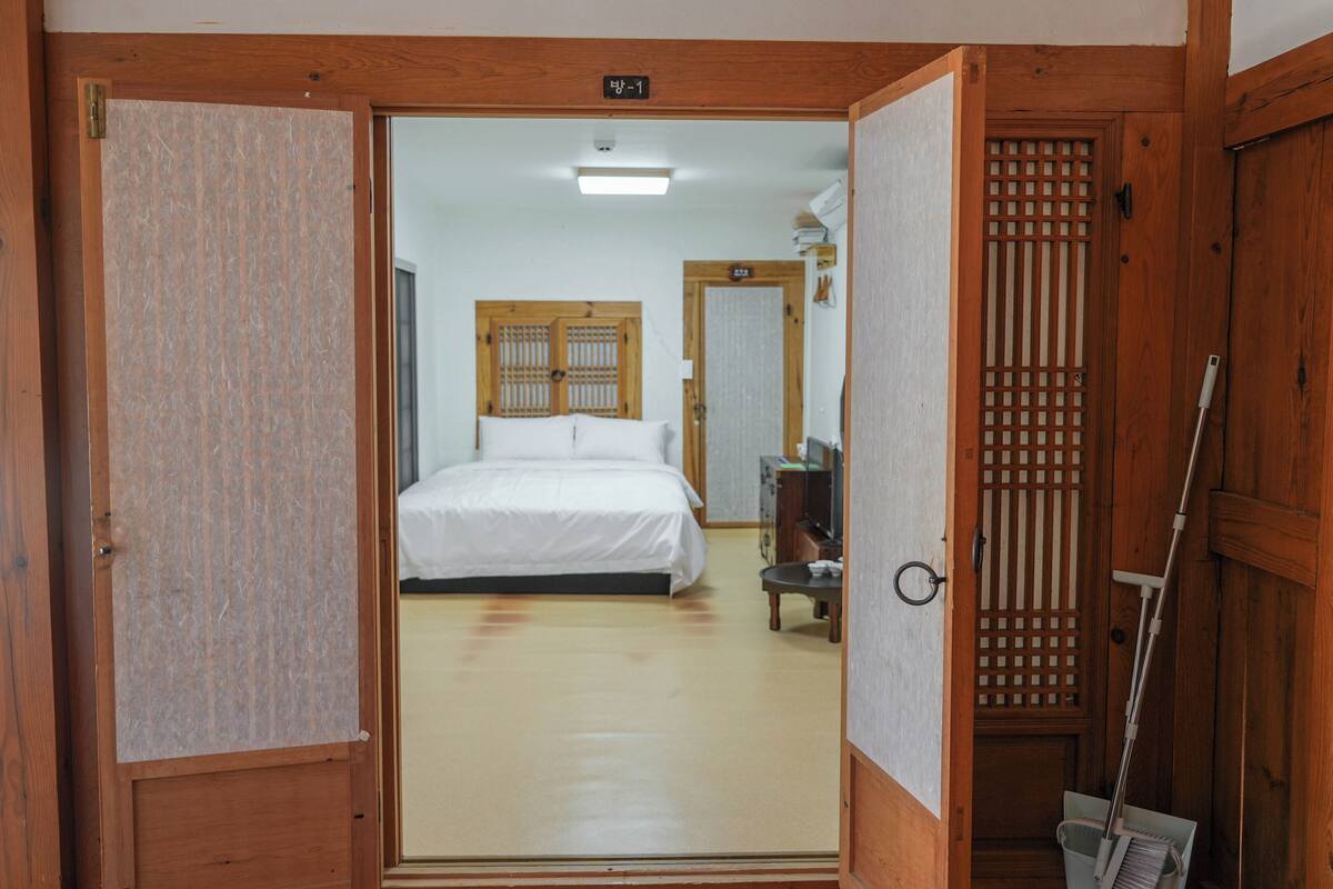 Een traditionele Japanse kamer met een houten vloer, een bed met witte beddengoed, een houten deur en een schuifdeur.