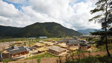 A traditional Korean village with wooden houses, a curved building, and mountains in the background.
