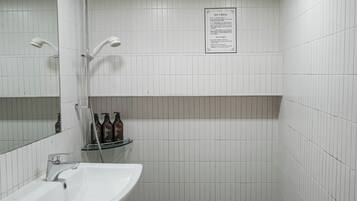 A bathroom with a sink, mirror, shower, and a shelf with bottles.