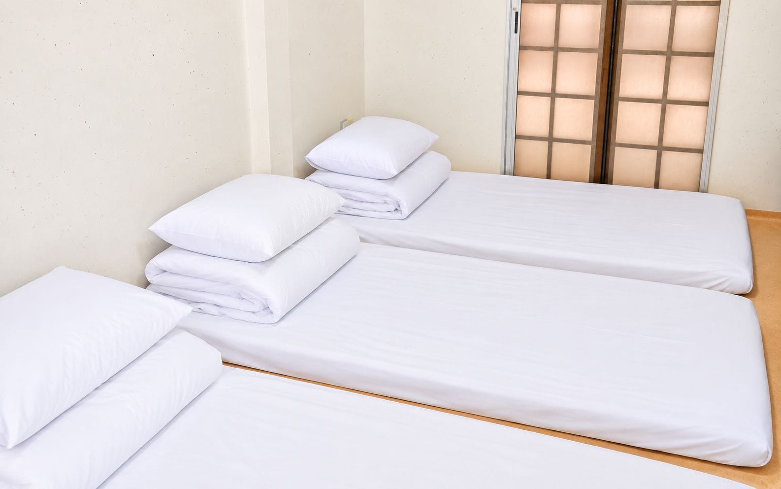 A room with three single beds, each with white bedding and pillows, and a wooden floor.