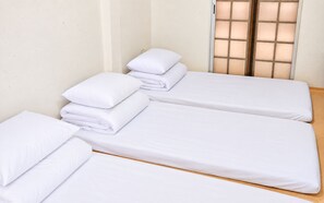 Une chambre avec trois lits simples, chacun doté de draps et d’oreillers blancs, et un plancher en bois.