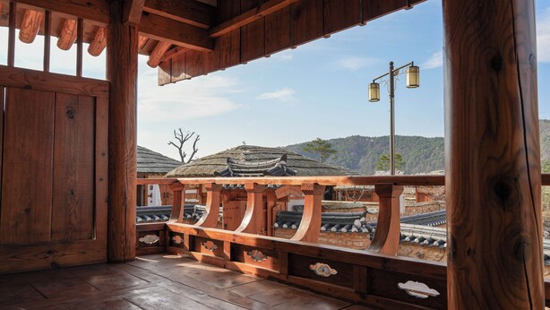 A wooden balcony with traditional architectural elements, a view of a temple, and a clear sky.