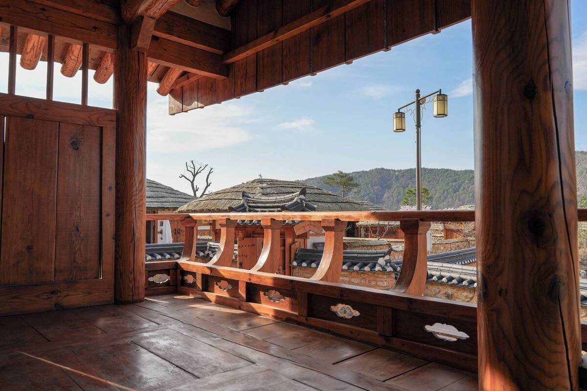 Een houten balkon met traditionele architectuurelementen, een uitzicht op een tempel en een heldere lucht.