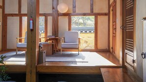 A traditional Japanese room with tatami flooring, a low wooden table, a cushioned chair, and a sliding door.