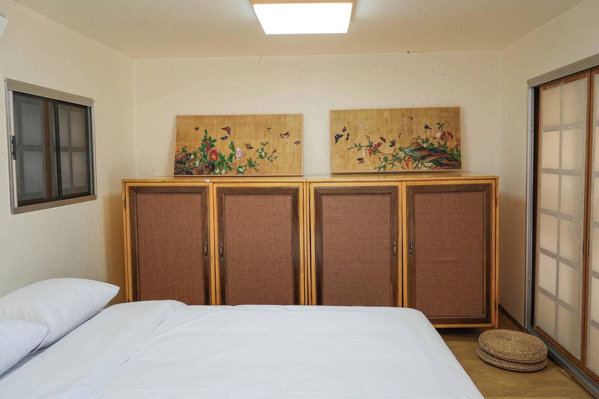 Een kamer met een bed, een raam, een schuifdeur en twee schilderijen aan de muur.
