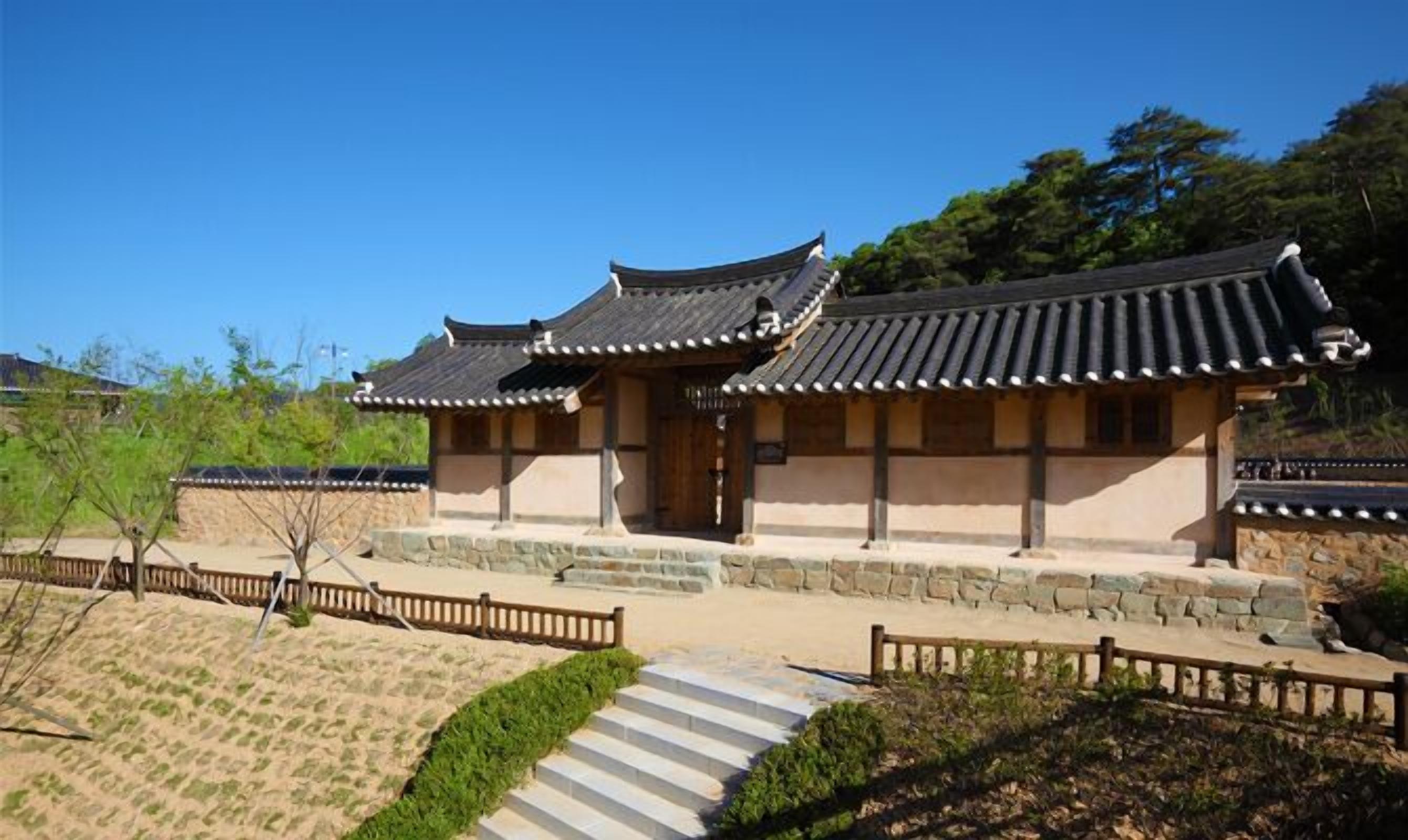 A traditional Korean building with a tiled roof, stone steps, and a wooden fence.