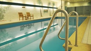 Une piscine intérieure offrant une vue dégagée sur le bassin, une échelle en métal et un mur orné de motifs de carreaux, ainsi que deux chaises en bois.