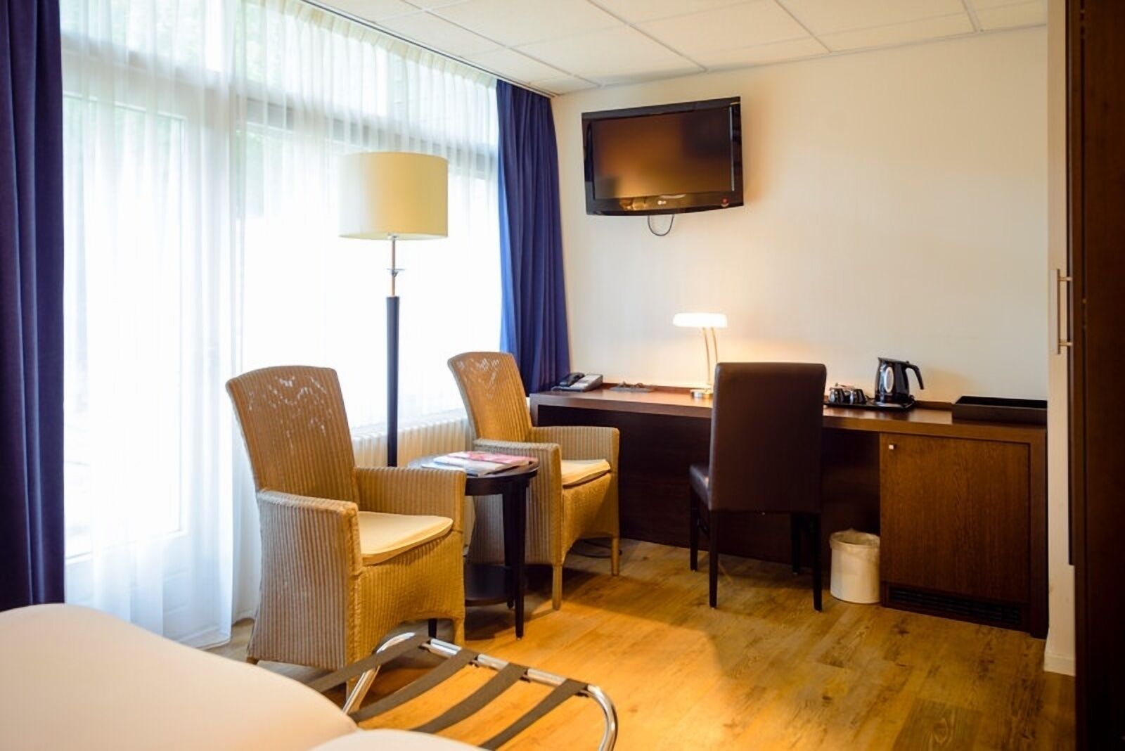 Une chambre d’hôtel avec un lit, deux chaises, un bureau, une télévision et une lampe.