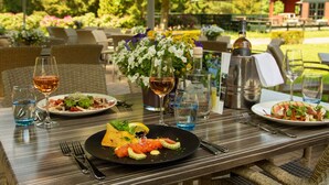Une table à manger installée à l’extérieur, avec des assiettes remplies de nourriture, des verres à vin et un vase de fleurs.