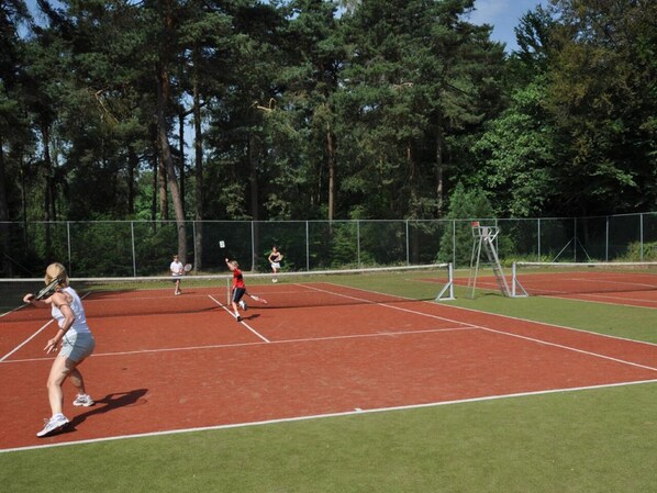 A tennis court with players, surrounded by trees.