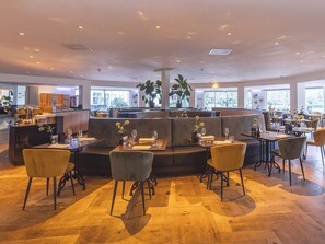 A spacious restaurant with high ceilings, wooden flooring, and a central seating area with sofas and chairs.